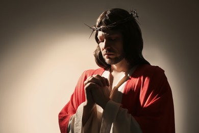 Jesus Christ with crown of thorns praying on light background, space for text
