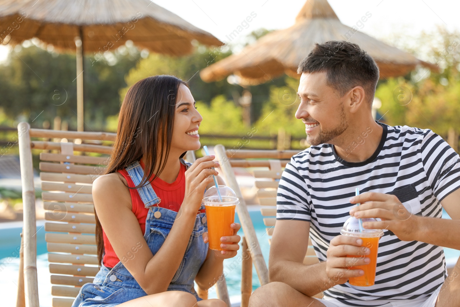 Image of Happy couple with cups of refreshing drink resting in deck chairs 