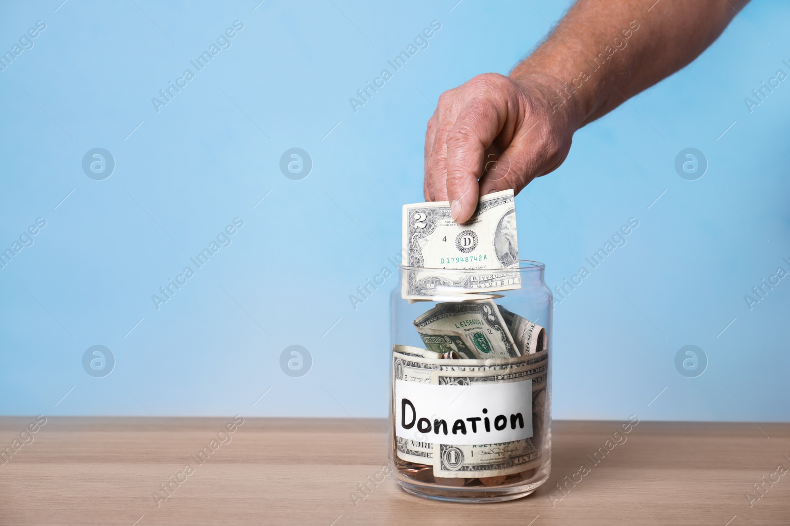 Photo of Man putting money into jar with label DONATION on table against color background, closeup. Space for text