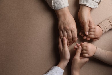 Photo of Family holding hands together on brown background, top view. Space for text