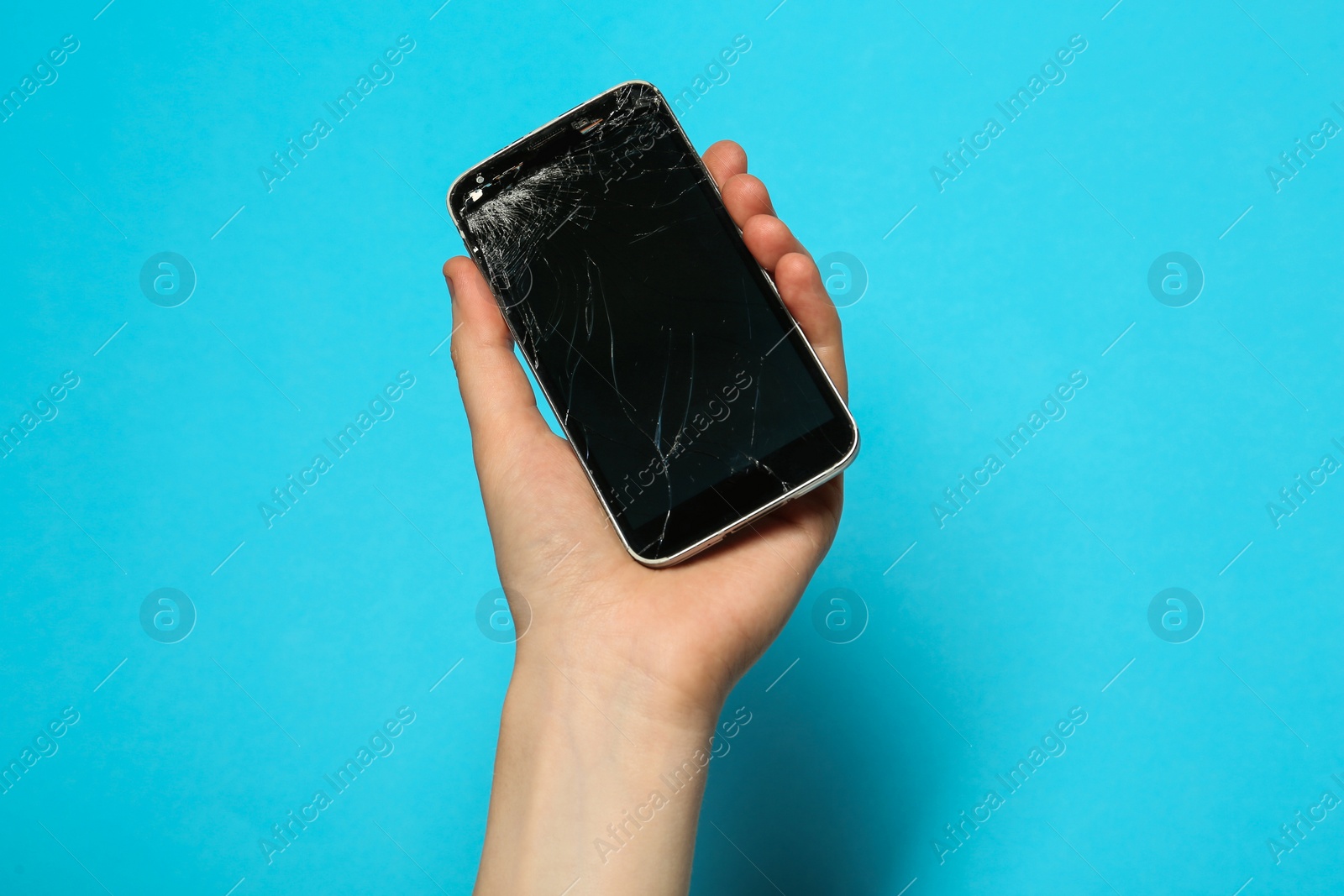 Photo of Woman holding damaged smartphone on light blue background, closeup. Device repairing