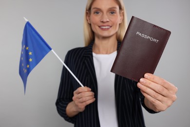 Photo of Immigration. Happy woman with passport and flag of European Union on gray background, selective focus