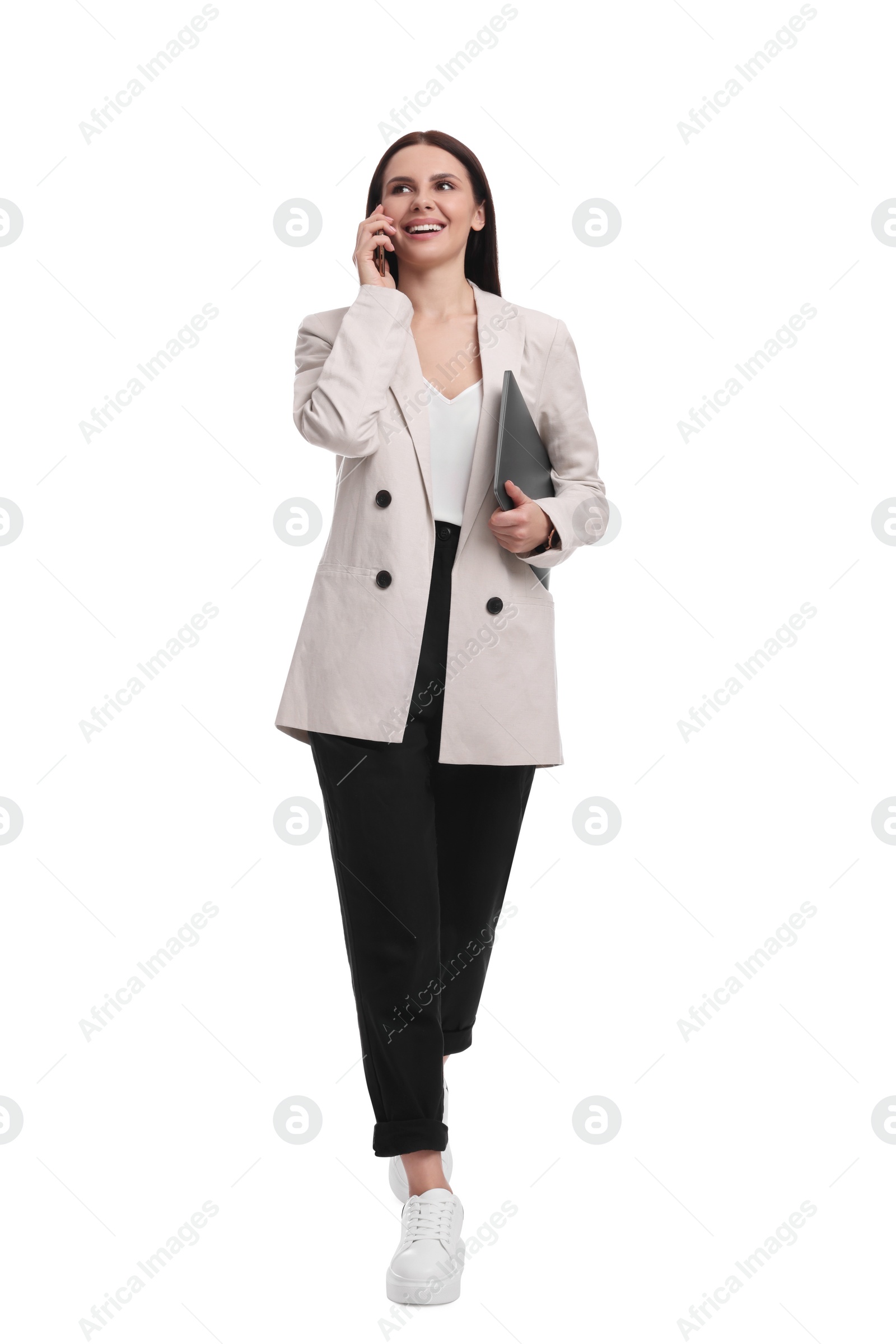 Photo of Beautiful businesswoman in suit with laptop talking on smartphone against white background