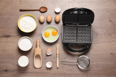 Flat lay composition with ingredients and Belgian waffle maker on wooden table