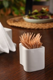 Photo of Holder with many toothpicks on wooden table, closeup