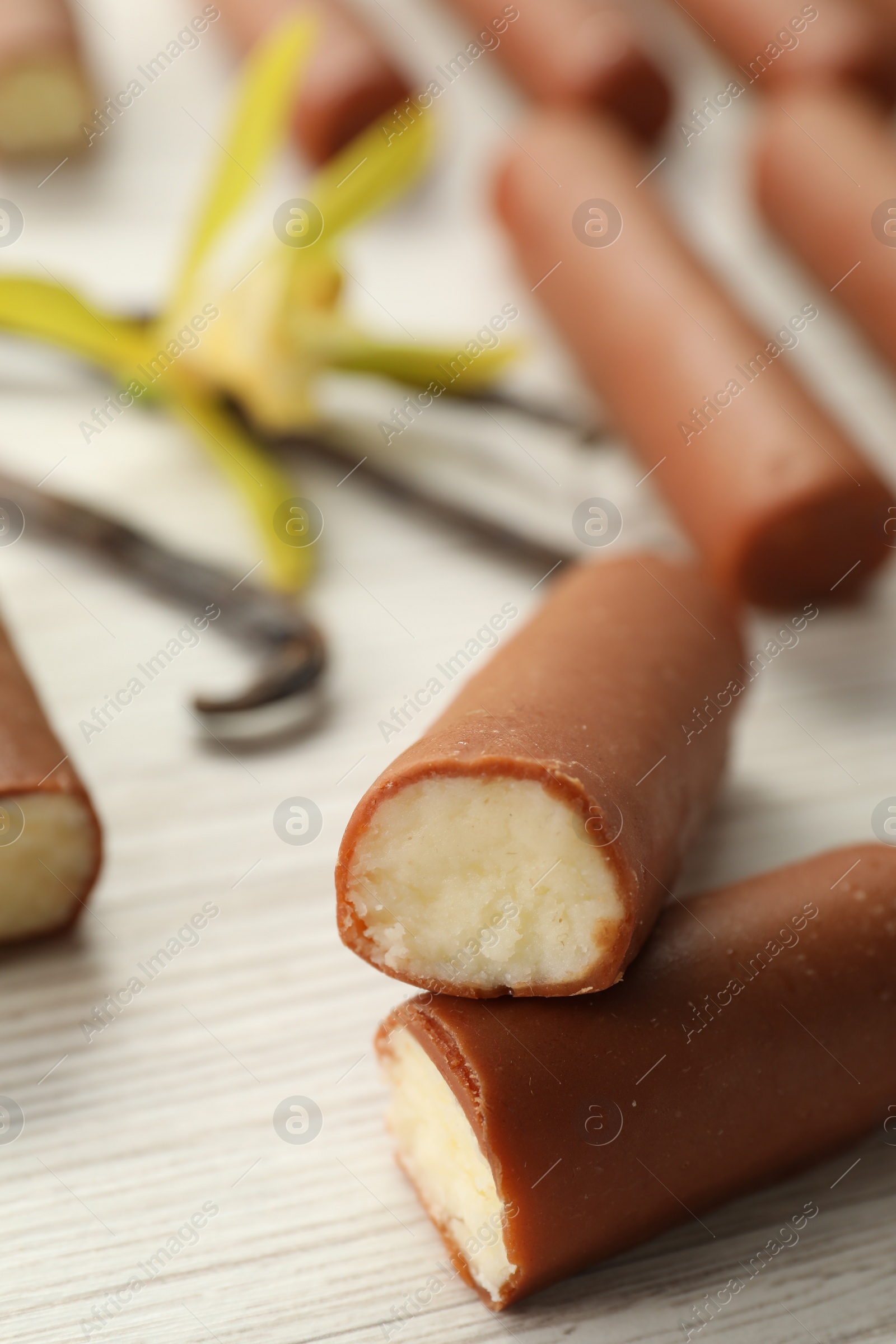 Photo of Glazed curd cheese bars, vanilla pods and flower on white wooden table, closeup