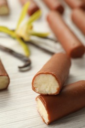 Glazed curd cheese bars, vanilla pods and flower on white wooden table, closeup