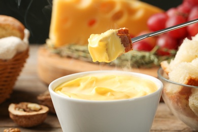 Photo of Piece of bread over bowl with delicious cheese fondue, closeup