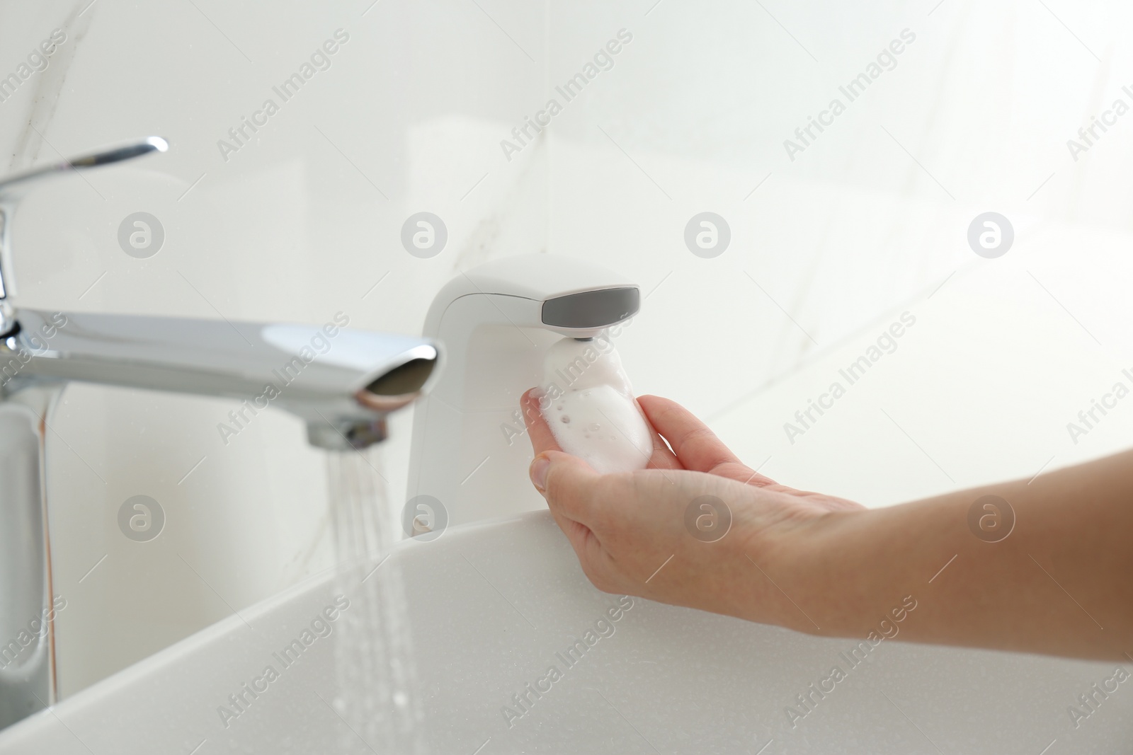 Photo of Woman using automatic soap dispenser in bathroom, closeup