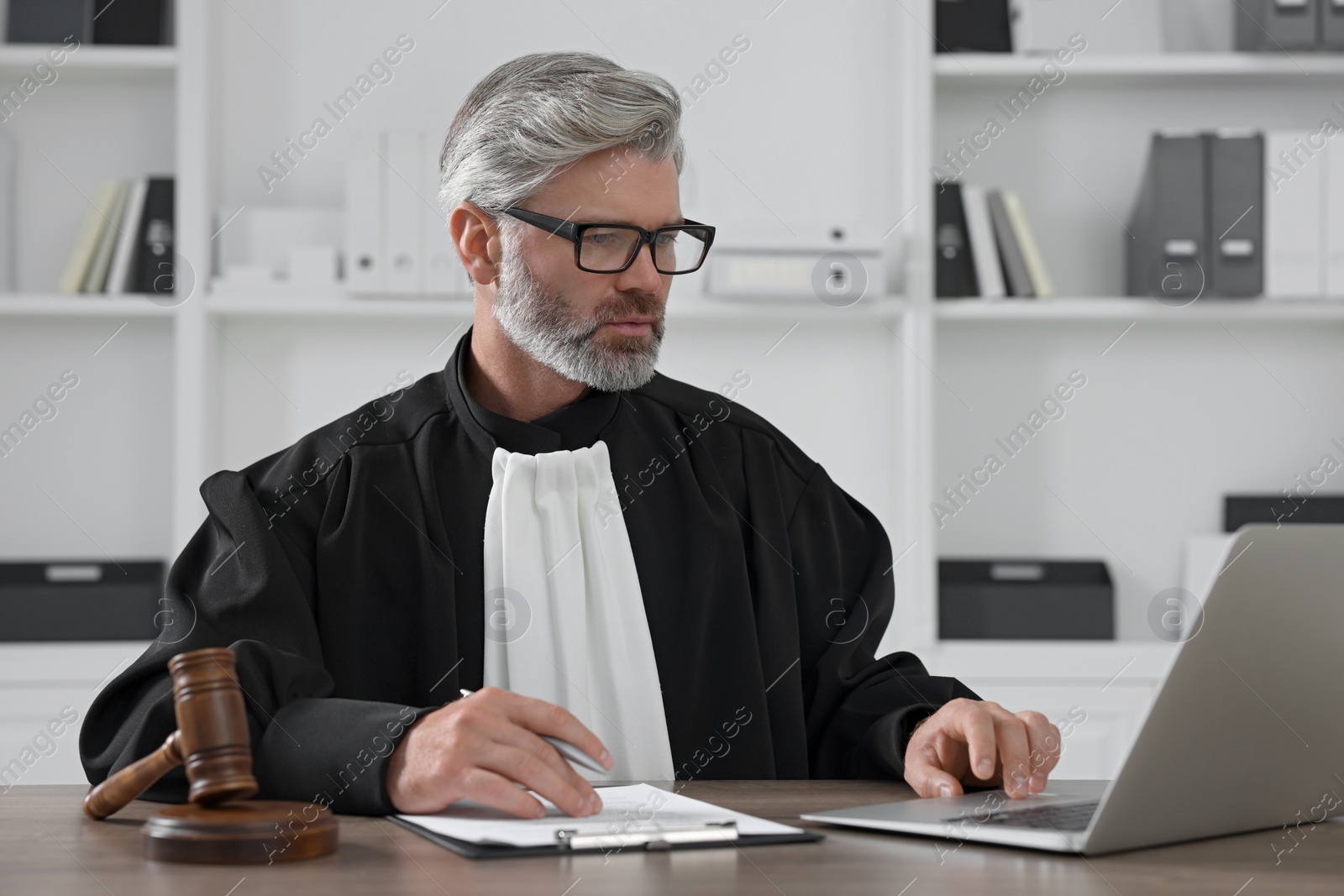 Photo of Judge with gavel, laptop and papers sitting at wooden table in office