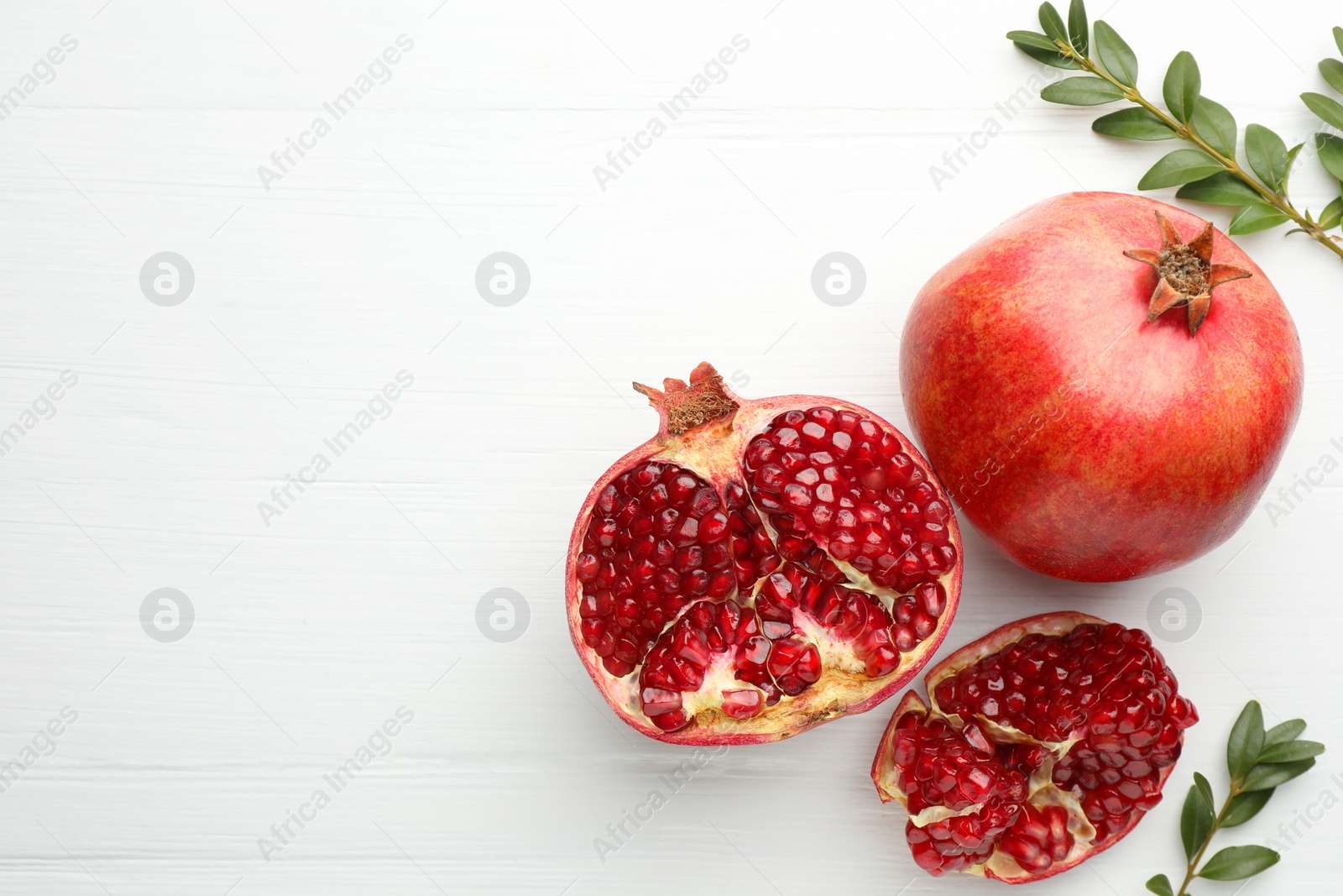 Photo of Fresh pomegranates and branches on white wooden table, flat lay. Space for text