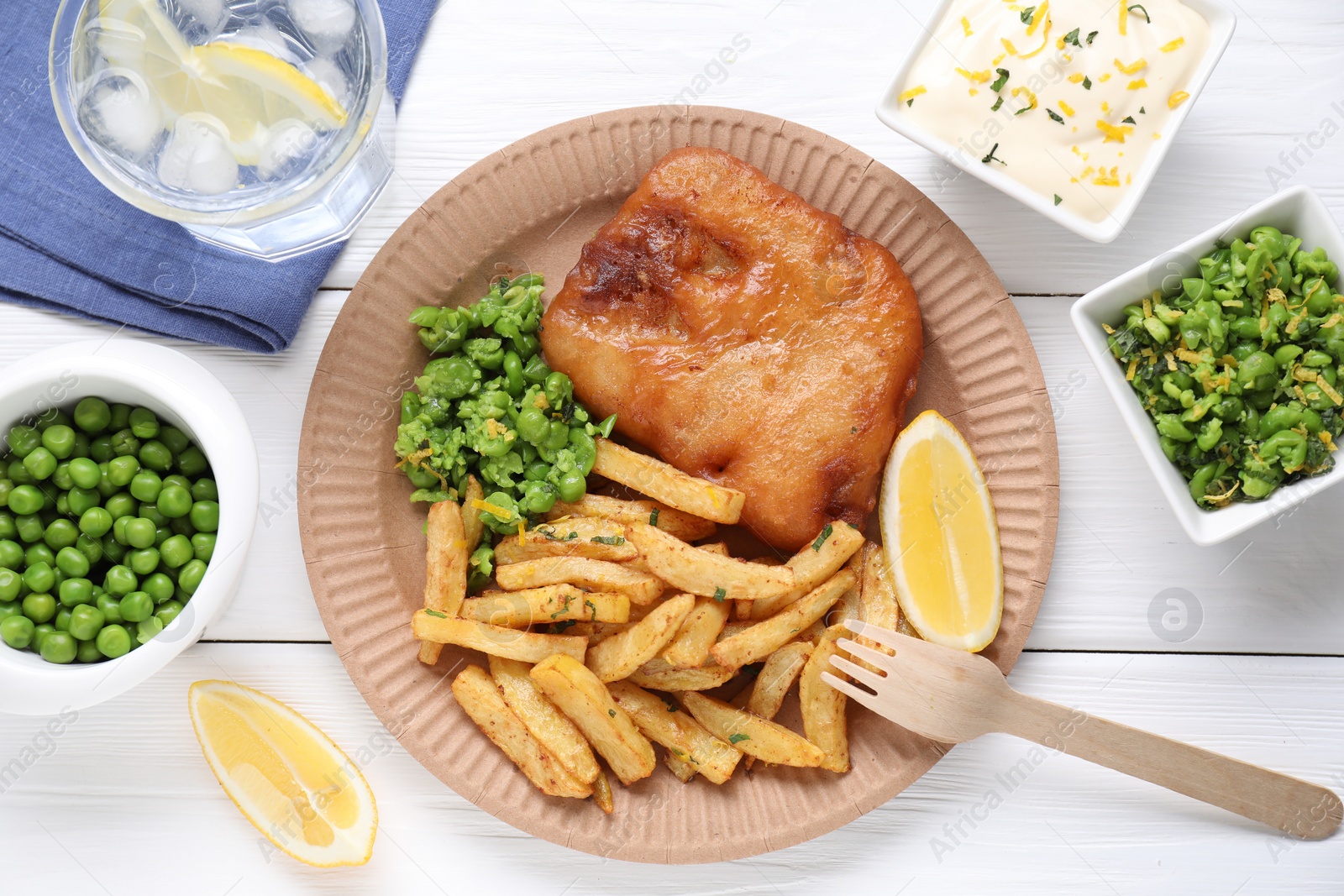 Photo of Tasty fish, chips, sauce, peas and lemon on white wooden table, top view