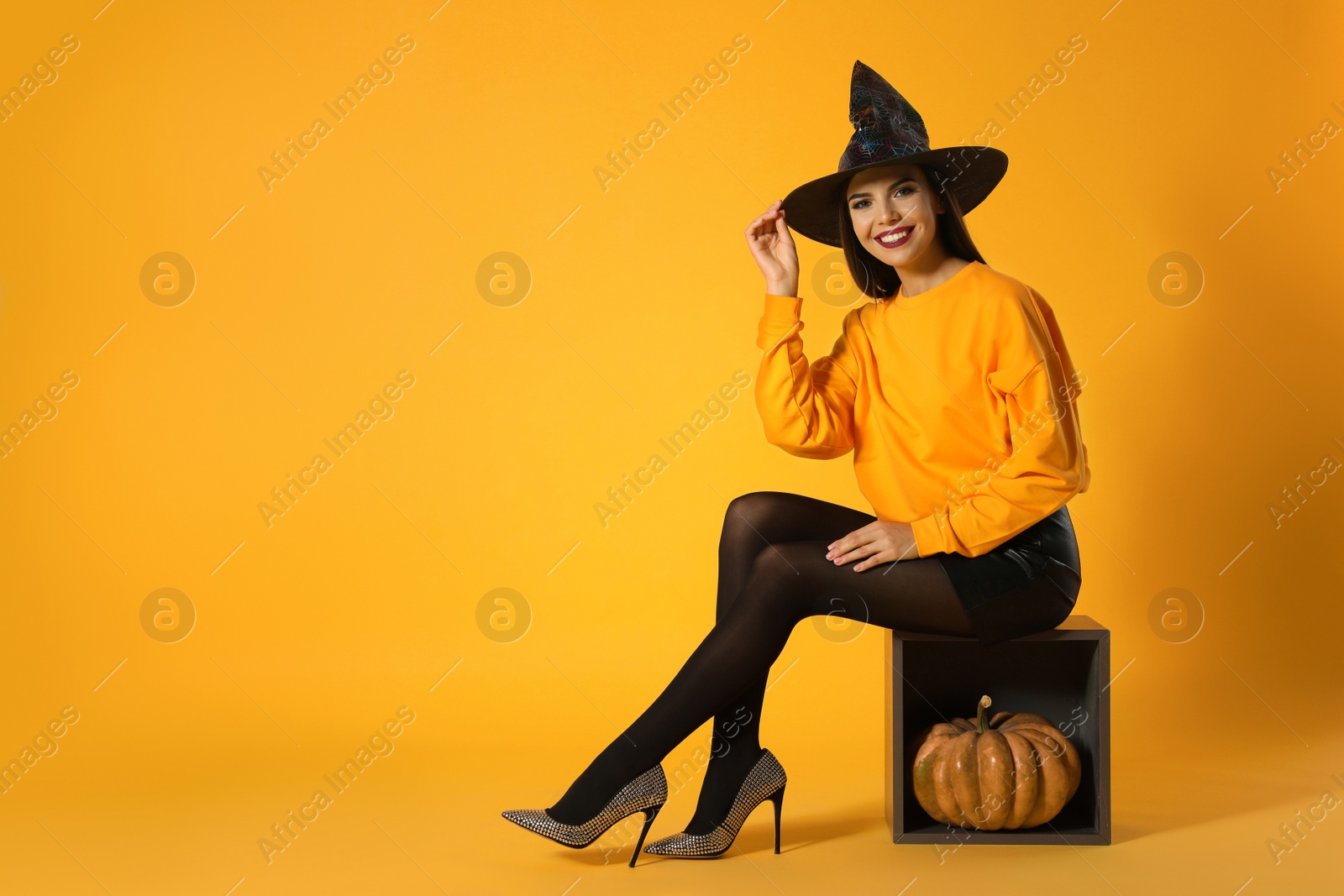 Photo of Beautiful woman wearing witch costume for Halloween party with pumpkin against yellow background, space for text