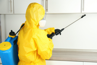 Pest control worker spraying pesticide in kitchen