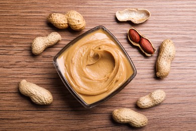 Yummy peanut butter in glass bowl on wooden table, flat lay