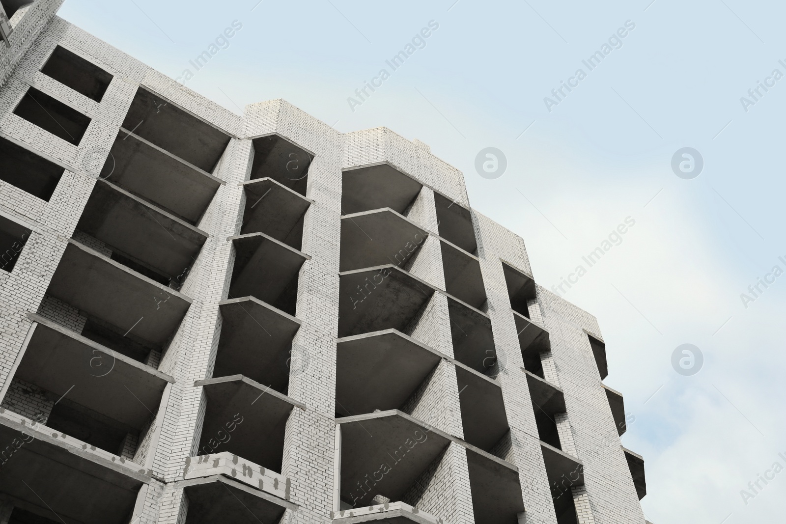 Photo of Construction site with unfinished building under cloudy sky, low angle view