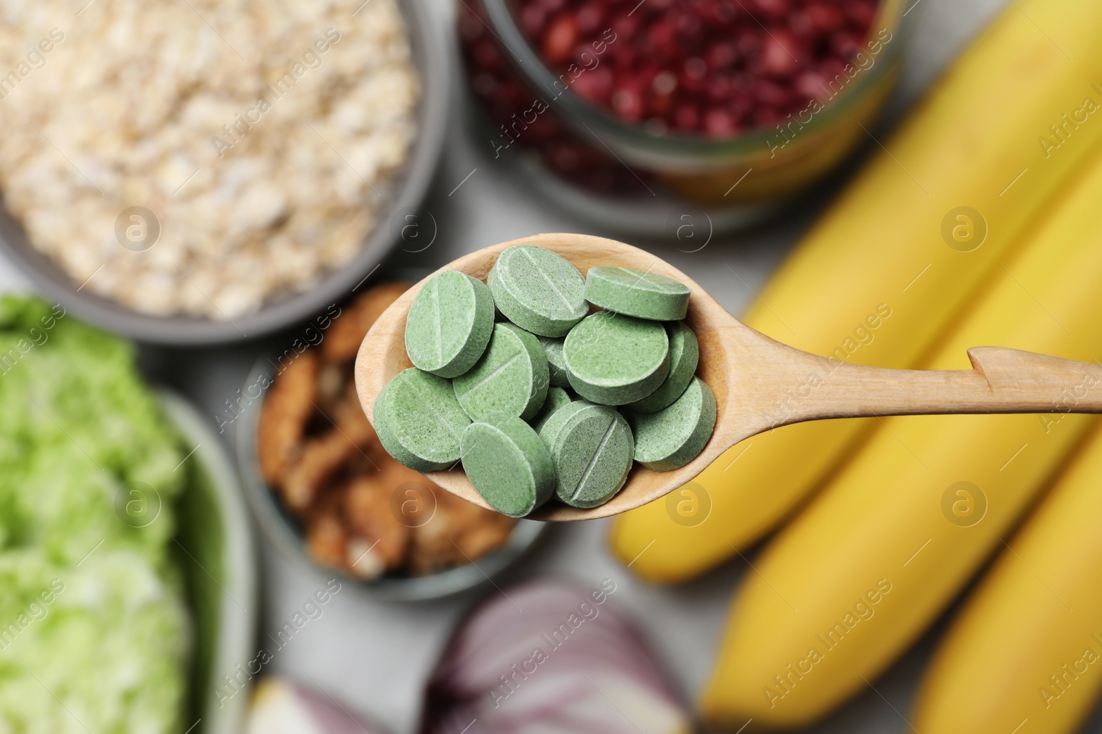 Photo of Wooden spoon of pills over table with foodstuff, top view. Prebiotic supplements