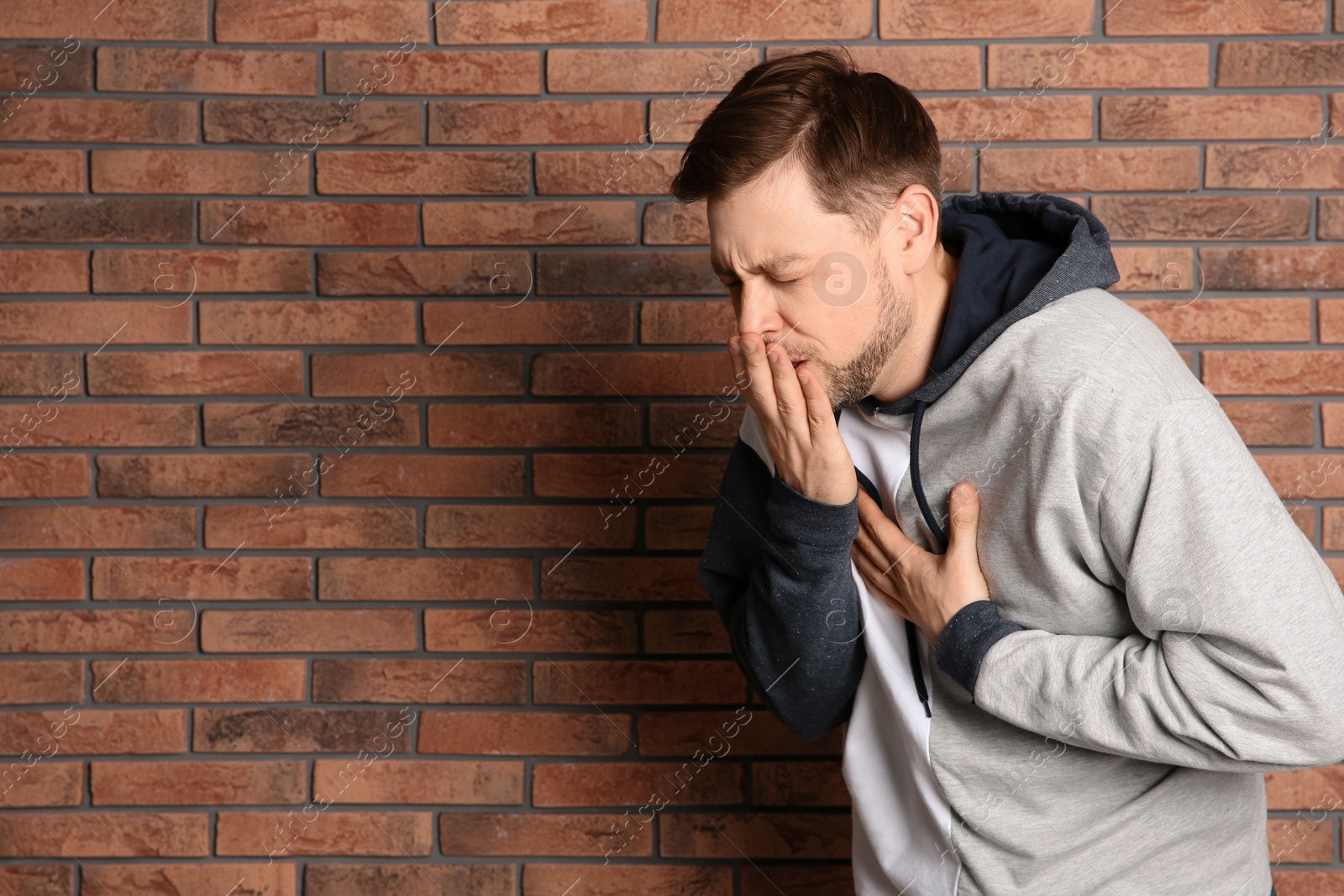 Photo of Man suffering from cough near brick wall. Space for text