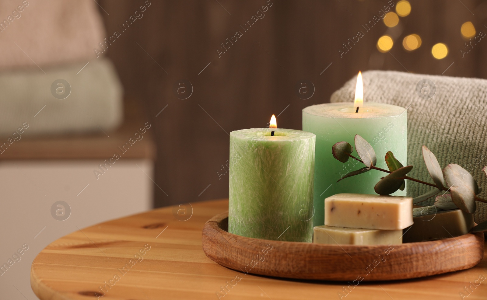 Photo of Spa composition. Burning candles, soap, towel and eucalyptus branch on wooden table, space for text