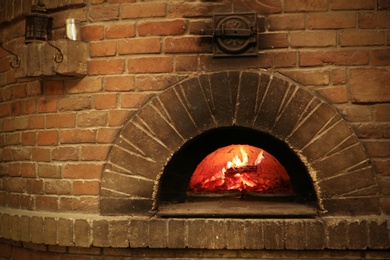 Photo of Brick oven with burning firewood and pizzas indoors