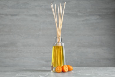 Photo of Aromatic reed freshener and kumquat on table against grey background