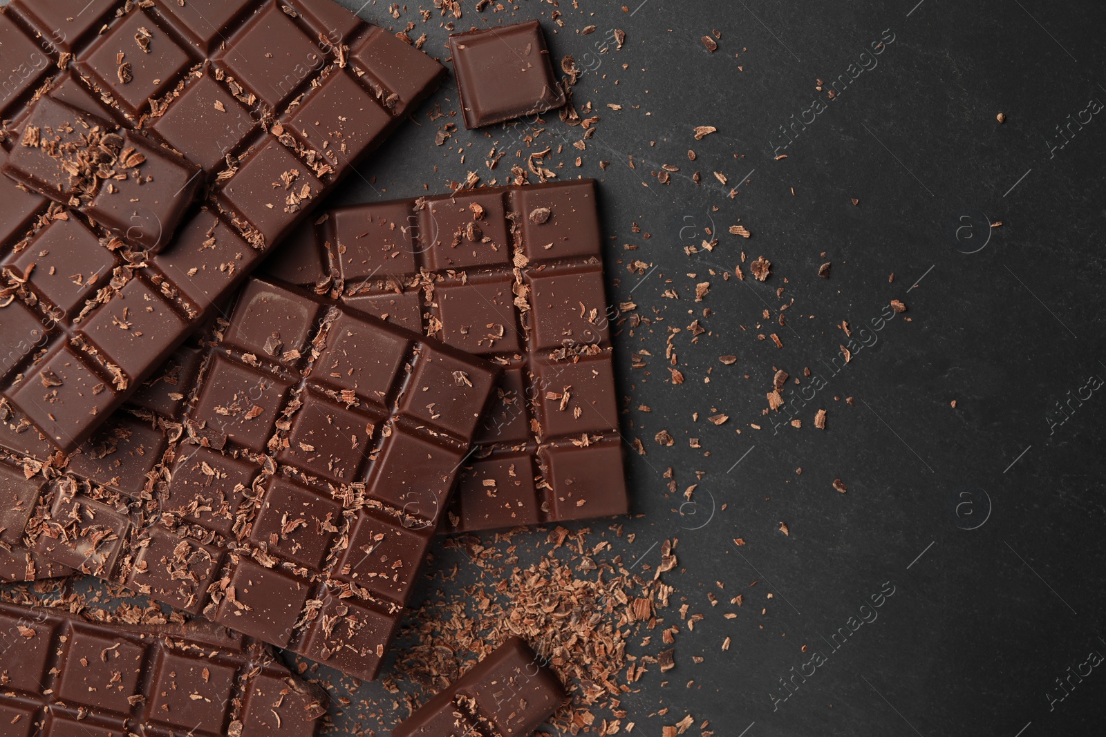 Photo of Pieces and shavings of tasty chocolate bars on grey table, flat lay. Space for text