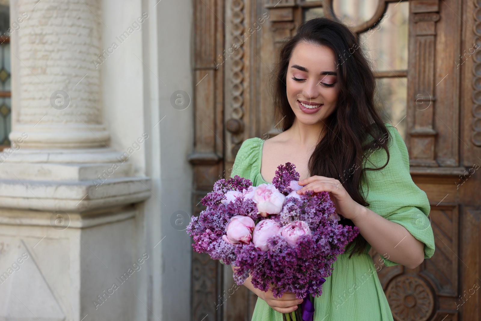 Photo of Beautiful woman with bouquet of spring flowers near building outdoors, space for text