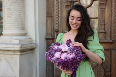 Photo of Beautiful woman with bouquet of spring flowers near building outdoors, space for text