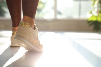 Photo of Young woman wearing stylish sneakers indoors, closeup