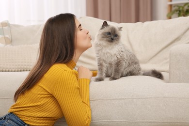 Woman kissing her cute cat near soft sofa at home