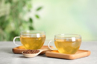 Photo of Cups of buckwheat tea and granules on table against blurred background. Space for text