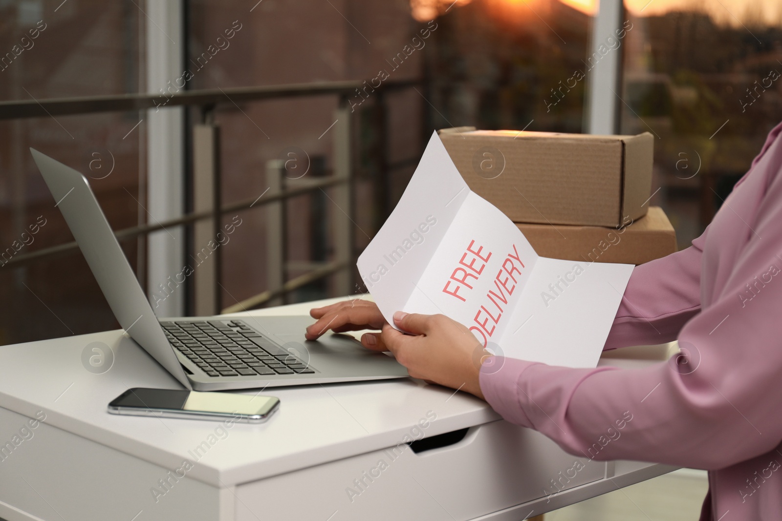 Photo of Woman with note Free Delivery working at table indoors, closeup. Courier service