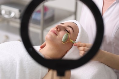 Photo of Cosmetologist making face massage with roller to client in clinic, closeup