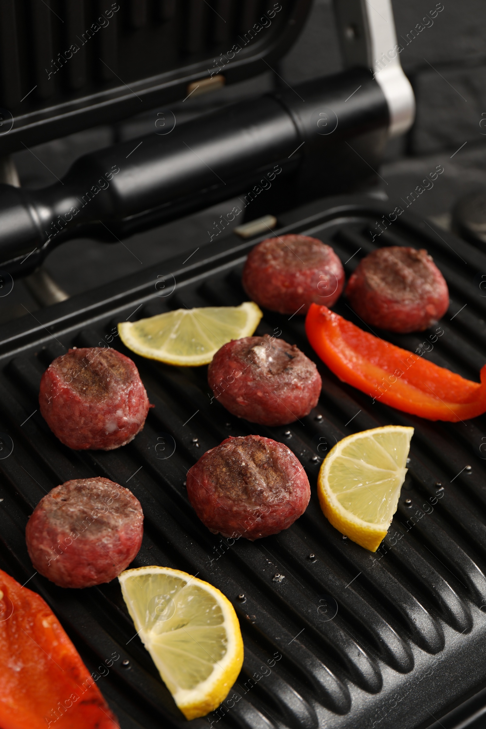 Photo of Electric grill with meat balls, bell pepper and lemon on table, closeup