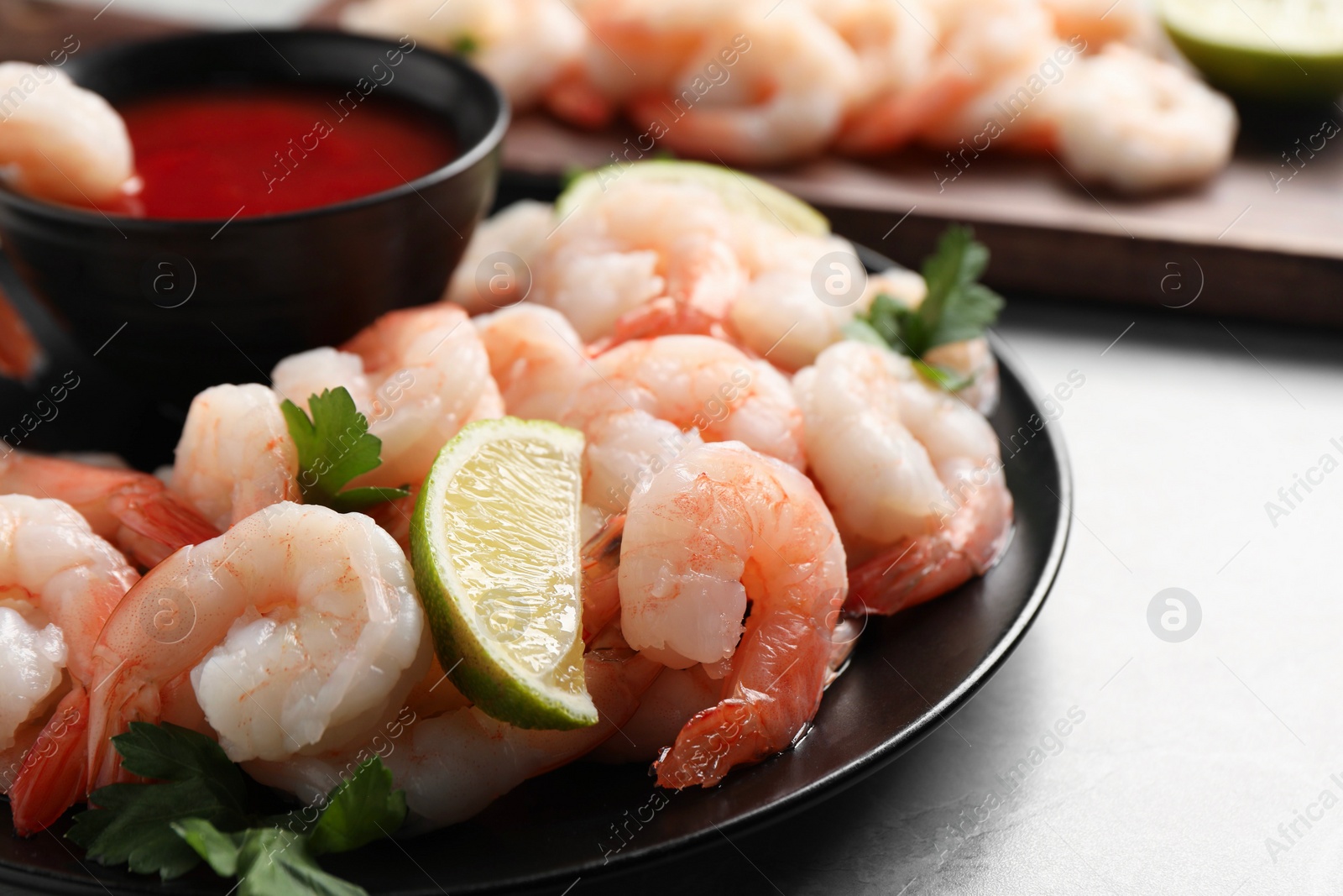 Photo of Tasty boiled shrimps with cocktail sauce, parsley and lime on light grey table, closeup