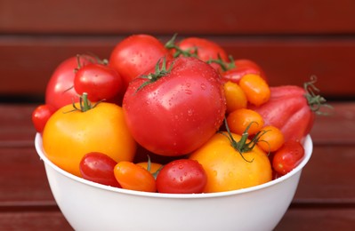 Bowl with fresh tomatoes on wooden table, closeup