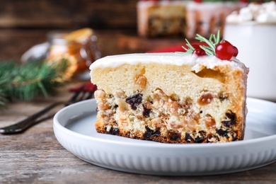 Slice of traditional Christmas cake decorated with rosemary and cranberries on wooden table, closeup