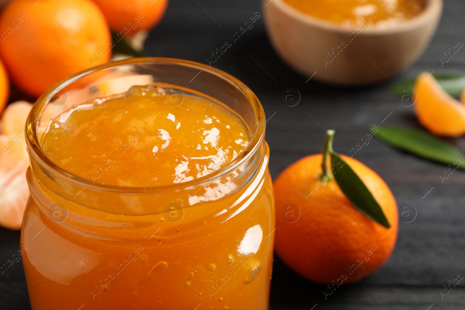 Photo of Tasty tangerine jam in glass jar on table, closeup. Space for text