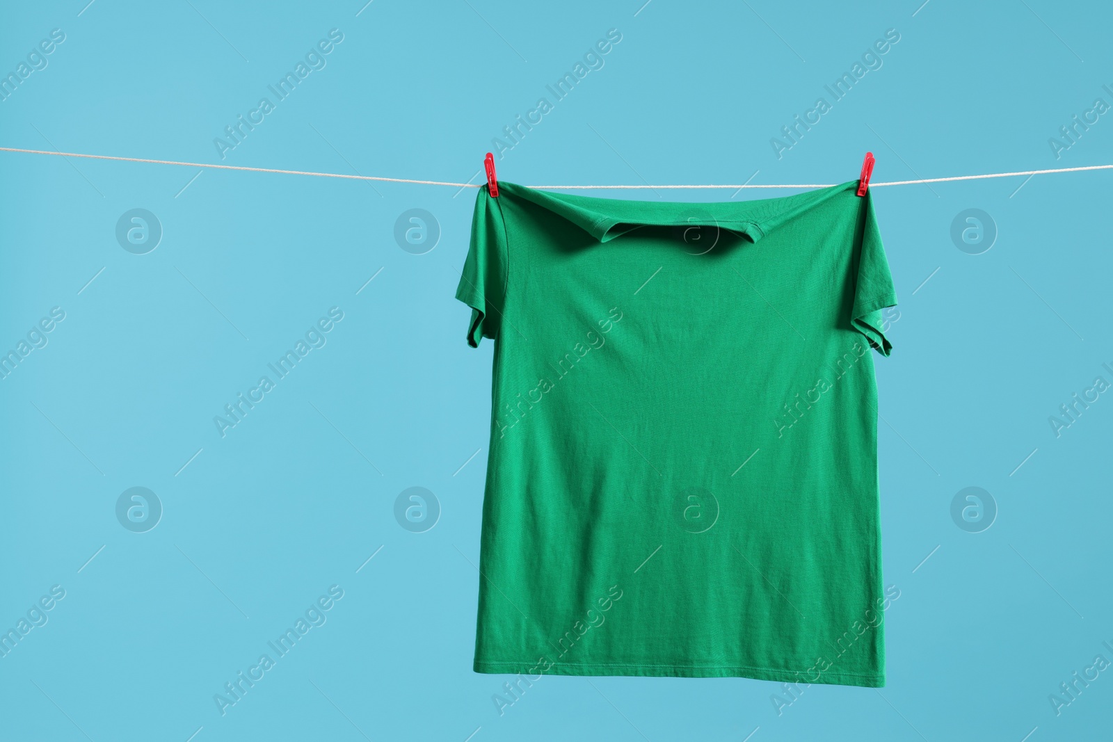 Photo of One green t-shirt drying on washing line against light blue background. Space for text