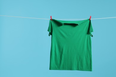 Photo of One green t-shirt drying on washing line against light blue background. Space for text