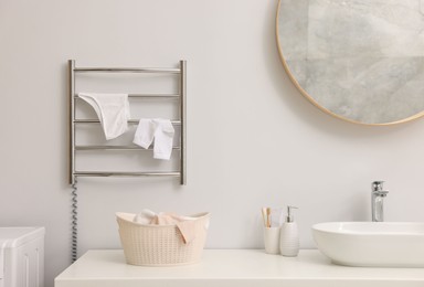 Photo of Heated towel rail with underwear and socks on white wall in bathroom