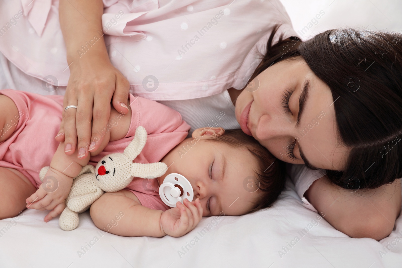 Photo of Young mother resting near her sleeping baby on bed