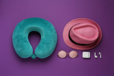 Photo of Turquoise travel pillow, hat, sunglasses and earphones on purple background, flat lay