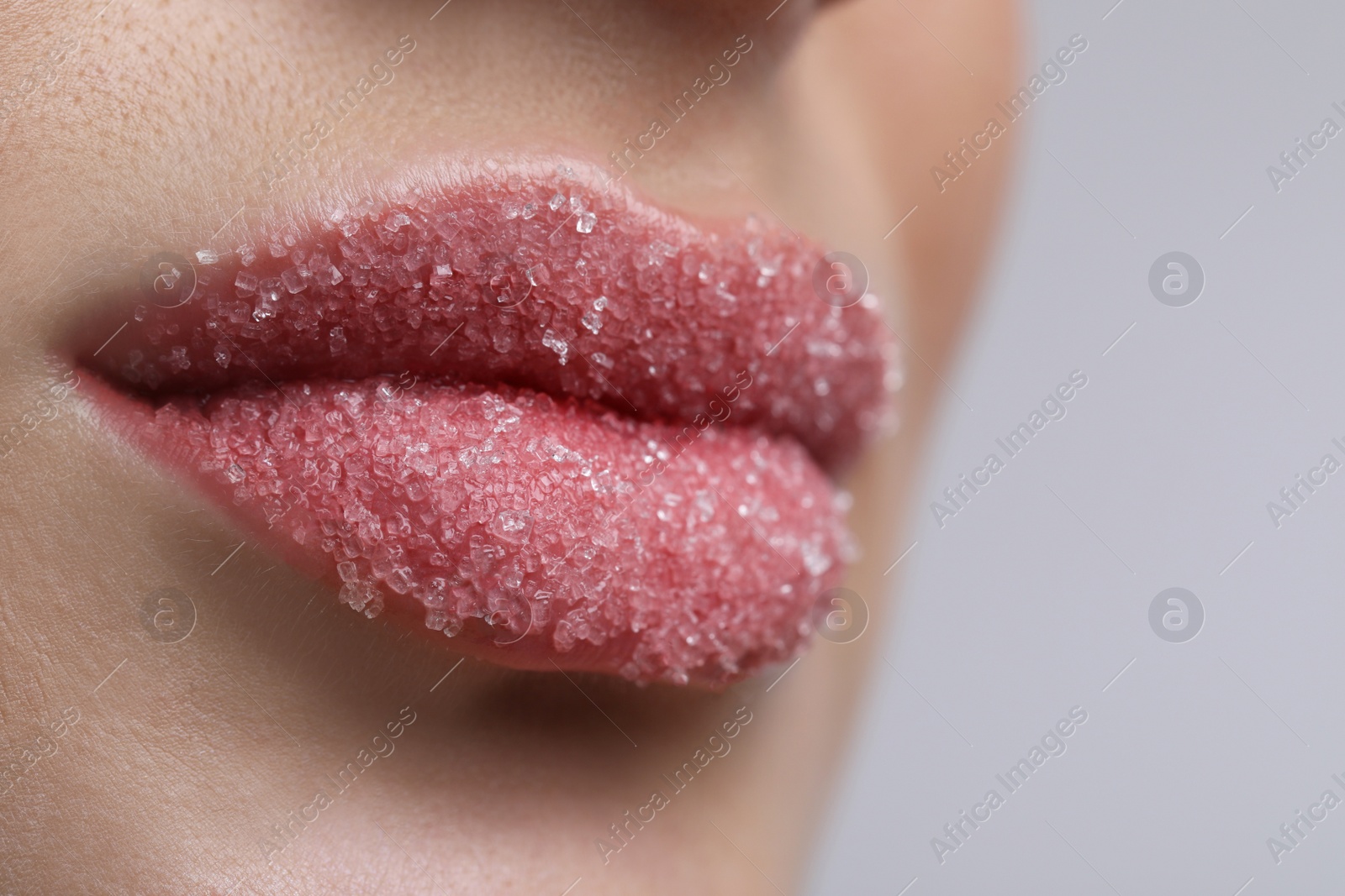 Photo of Young woman with beautiful lips covered in sugar on light background, closeup