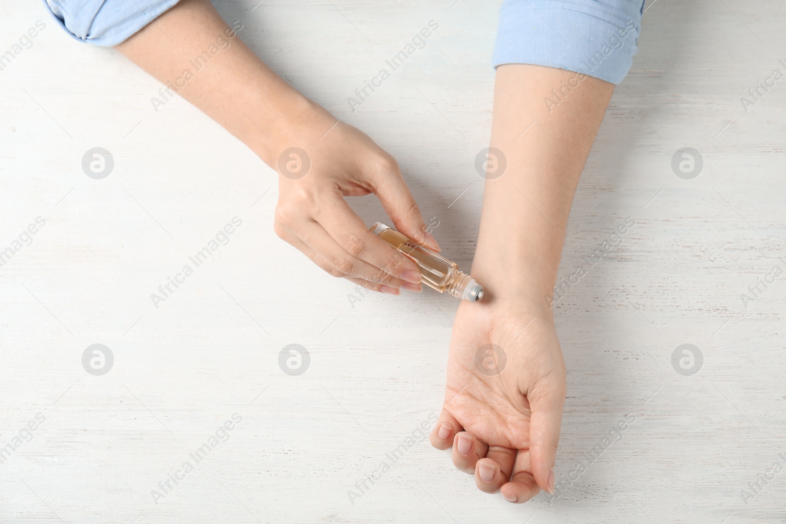 Photo of Woman applying essential oil on her wrist against white wooden background, top view. Space for text