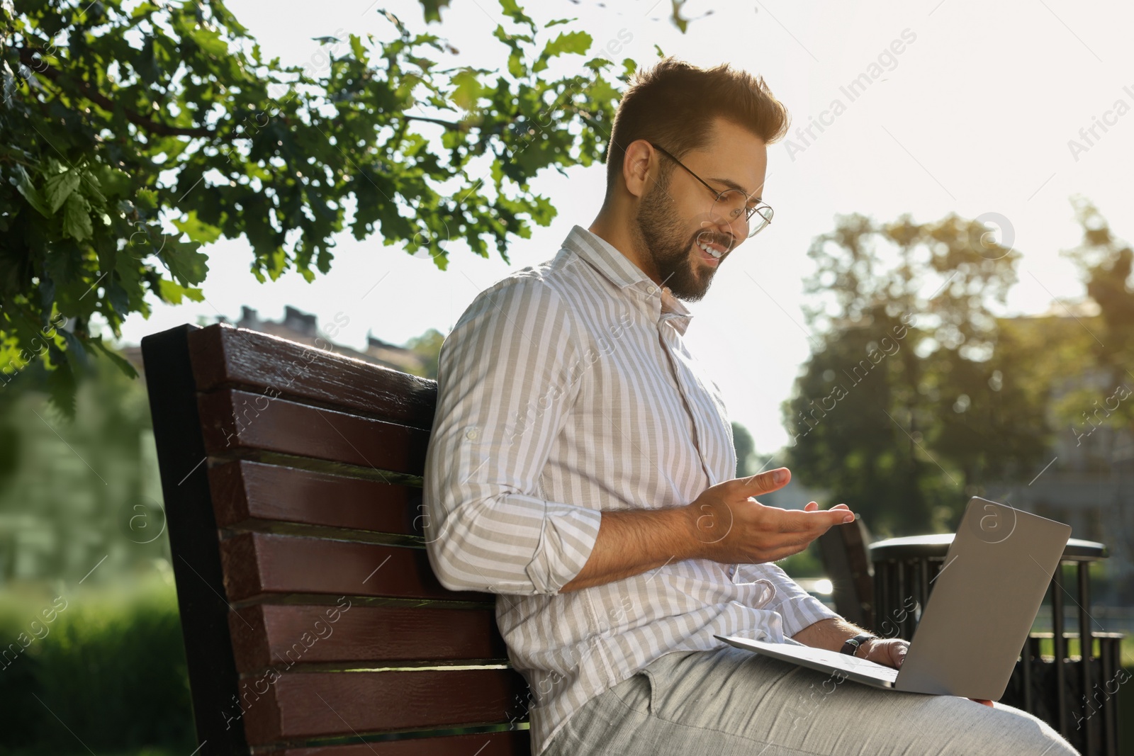 Photo of Young man using laptop on bench in park