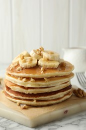 Photo of Delicious pancakes with bananas, walnuts and honey on white marble table