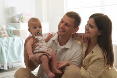 Happy couple and their cute little baby with pacifier at home