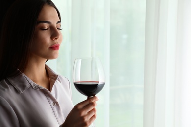 Photo of Beautiful young woman with glass of luxury red wine indoors. Space for text