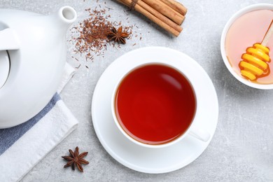 Photo of Freshly brewed rooibos tea, scattered dry leaves, honey and spices on grey table, flat lay